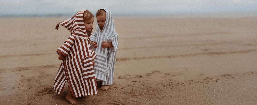 Two children in striped hooded ponchos on the beach